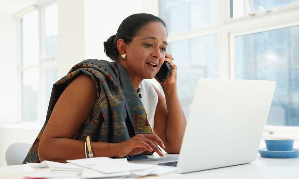 Woman talking on phone while working on laptop in office