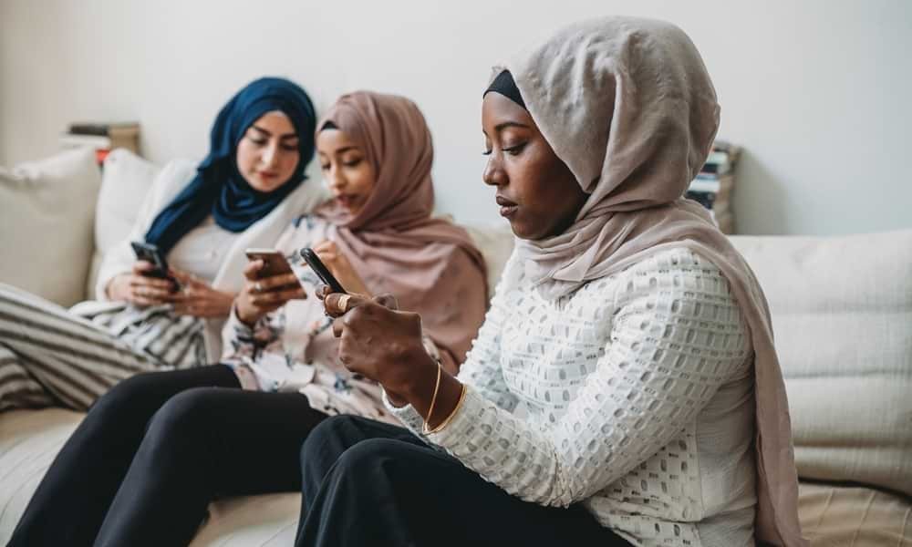 Black woman in hijab sitting on couch and looking at phone